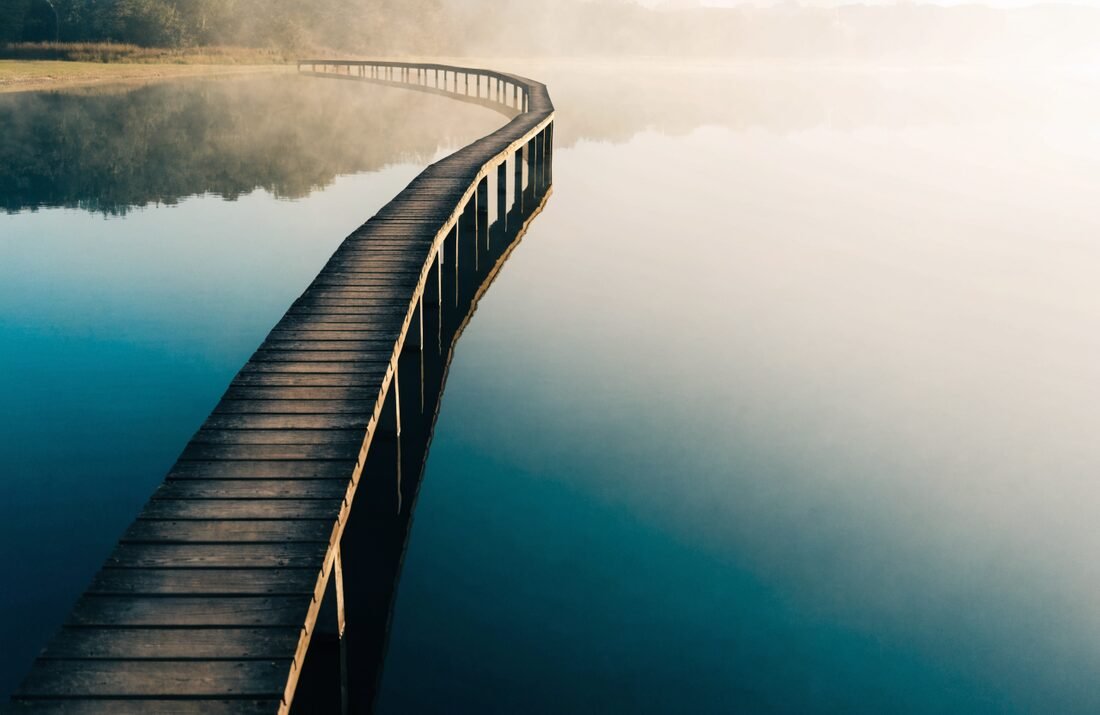 Ponte de madeira cruzando água calma ao amanhecer, arte-conceito sobre integração